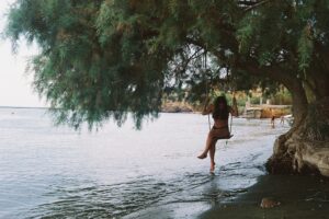 girl on swing under tree sea ocean thinking bathing suit